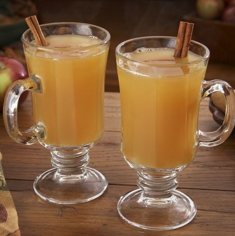steaming hot apple cider on a table with apples and ginger cookies
