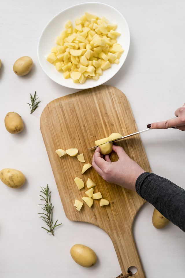 hands of woman chopping potatoes on cutting board