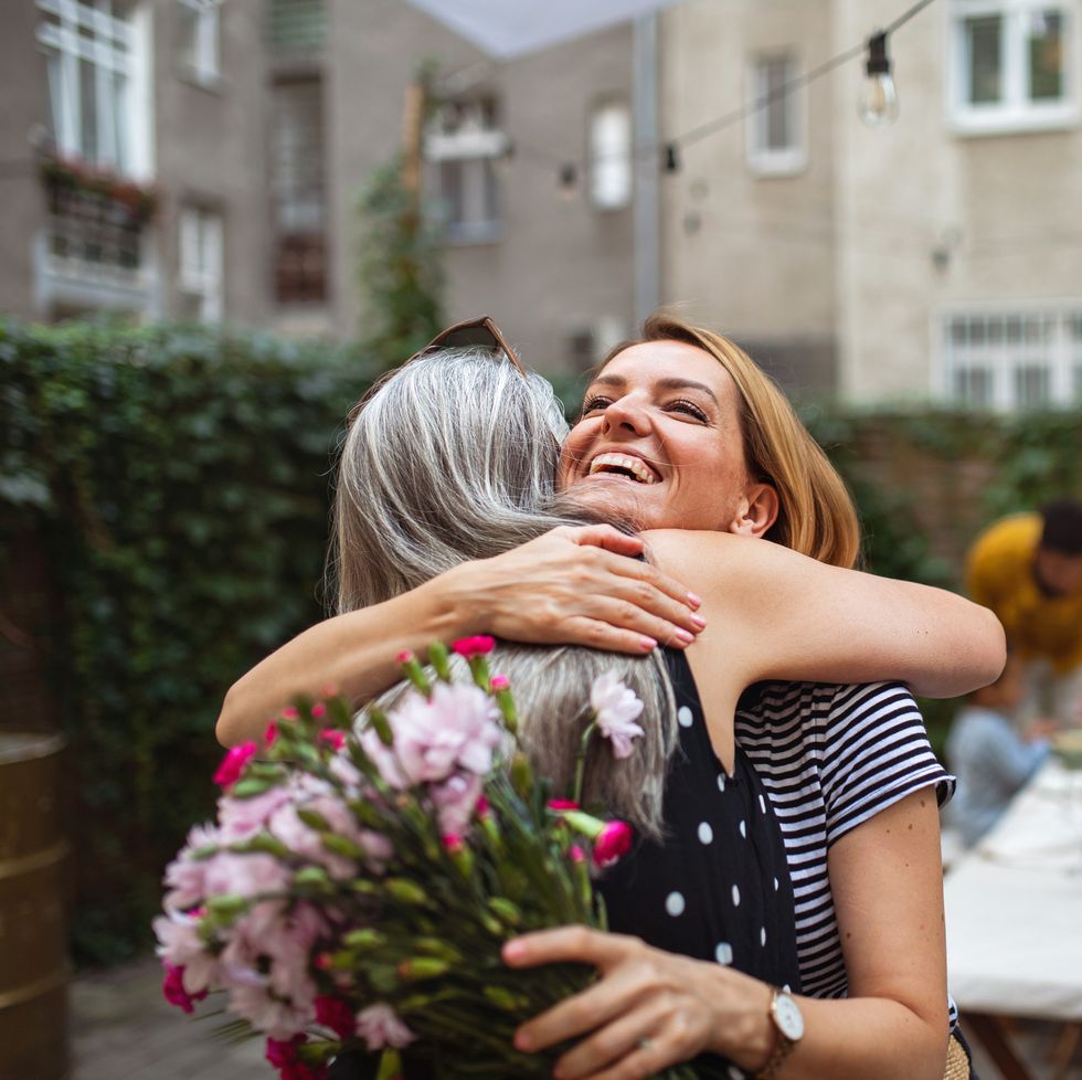 happy adult daughter with bouquet hugging her senior mother outdoors in garden