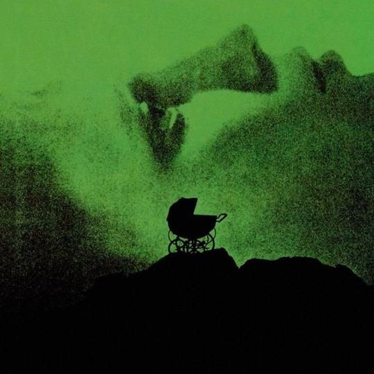 a baby carriage sits on top of an ominous craggy surface with a green glow and the face of roesmary behind it in the poster for rosemary's baby a good housekeeping pick for best halloween movies