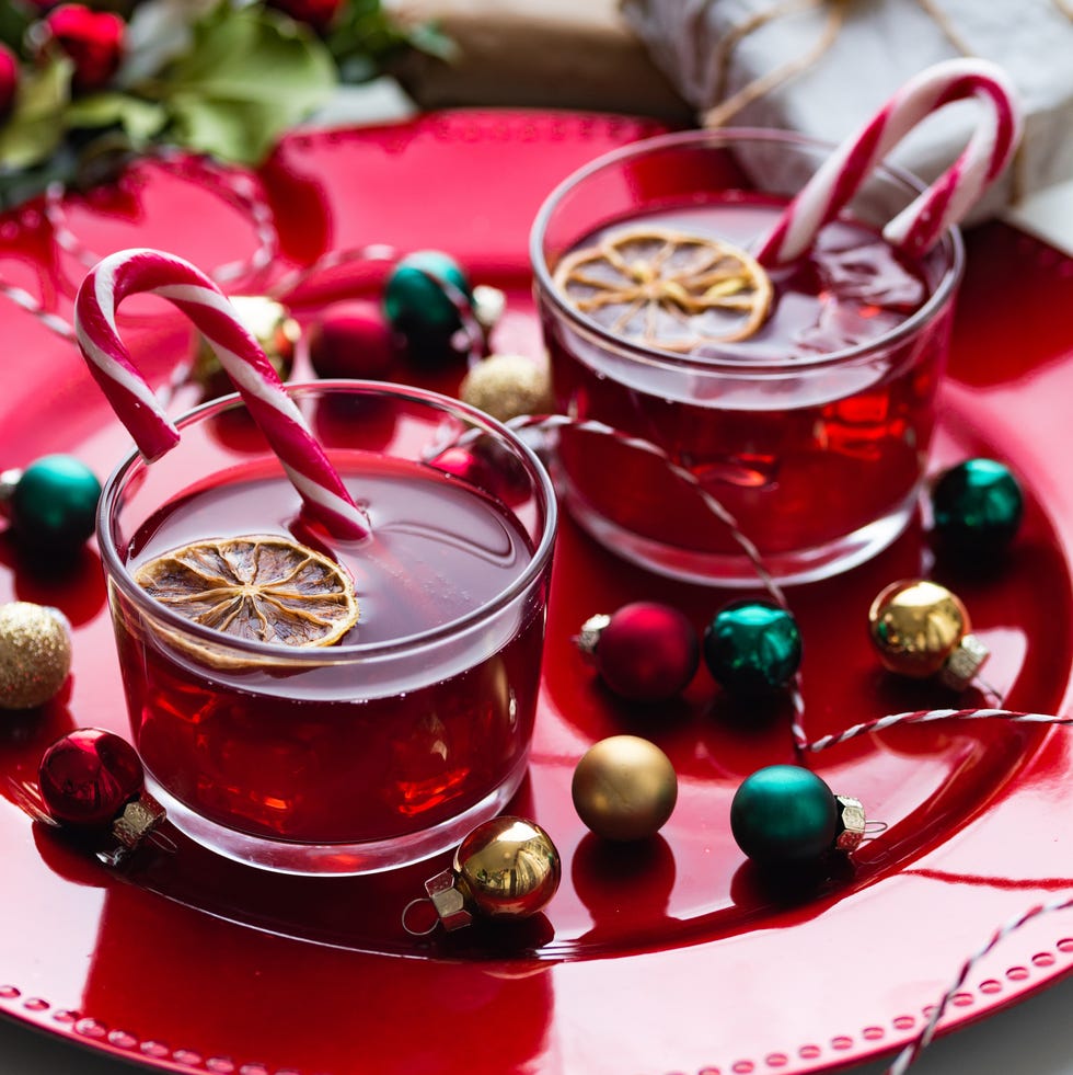 a couple of cups filled with mulled wine with candy canes sticking out of them sitting on a red plate surrounded by mini ornaments and holly leaves