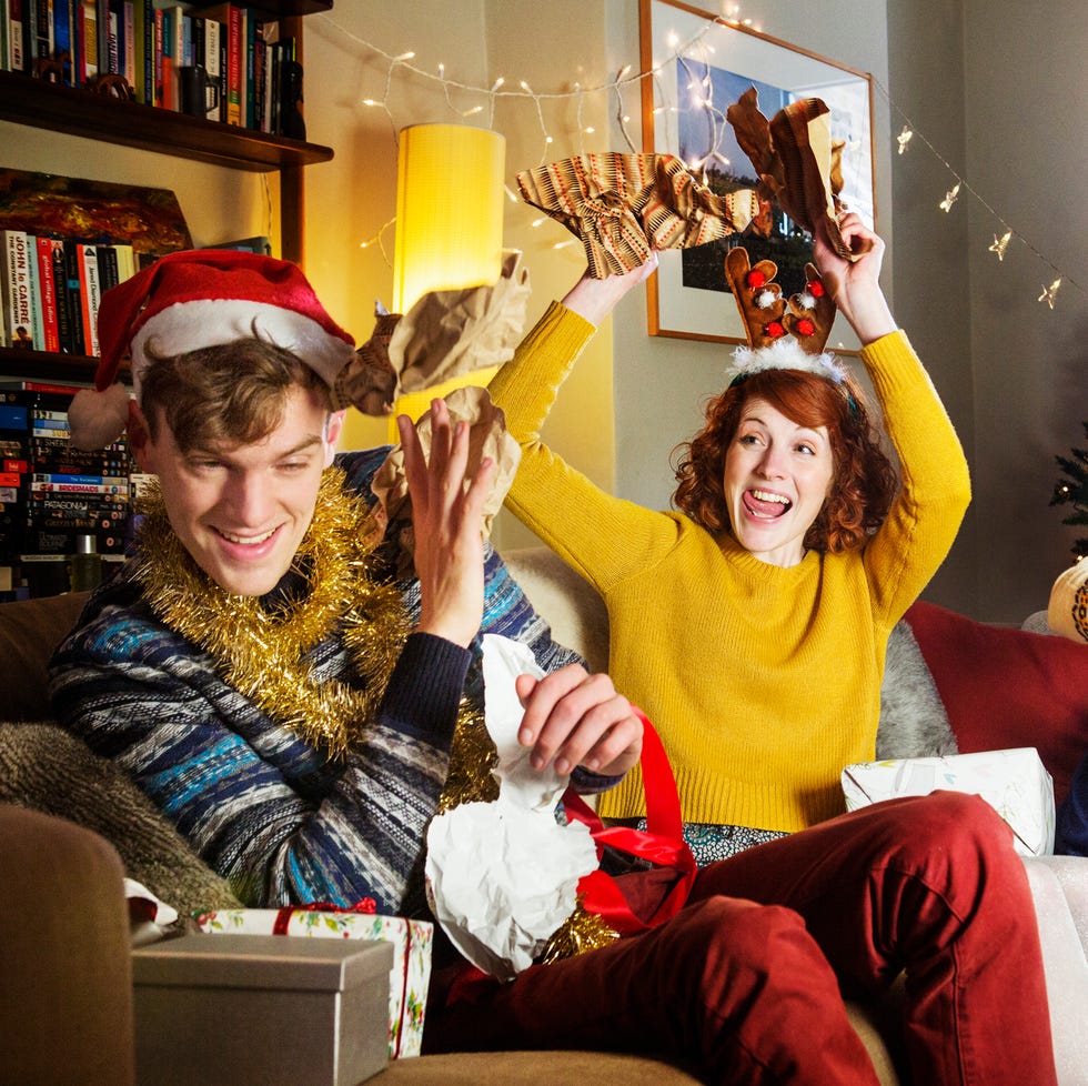 group of friends in christmas accessories sitting around talking and opening christmas gifts together