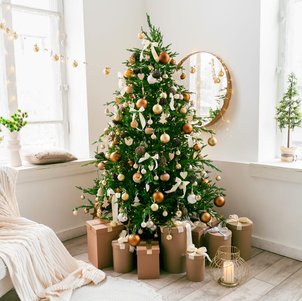 white and spacious domestic living room decorated with a christmas fir tree with ornaments in shades of gold on it