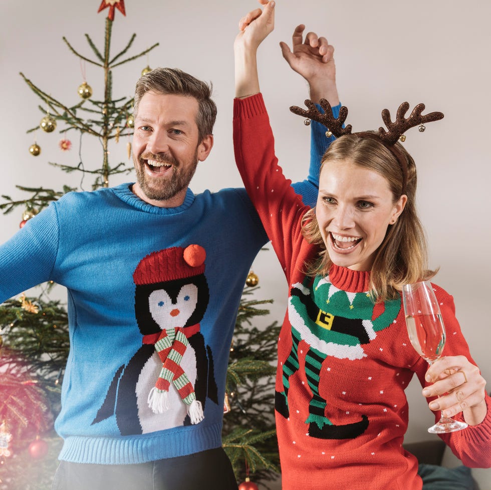 two adults in ugly christmas sweaters holding glasses of champagne