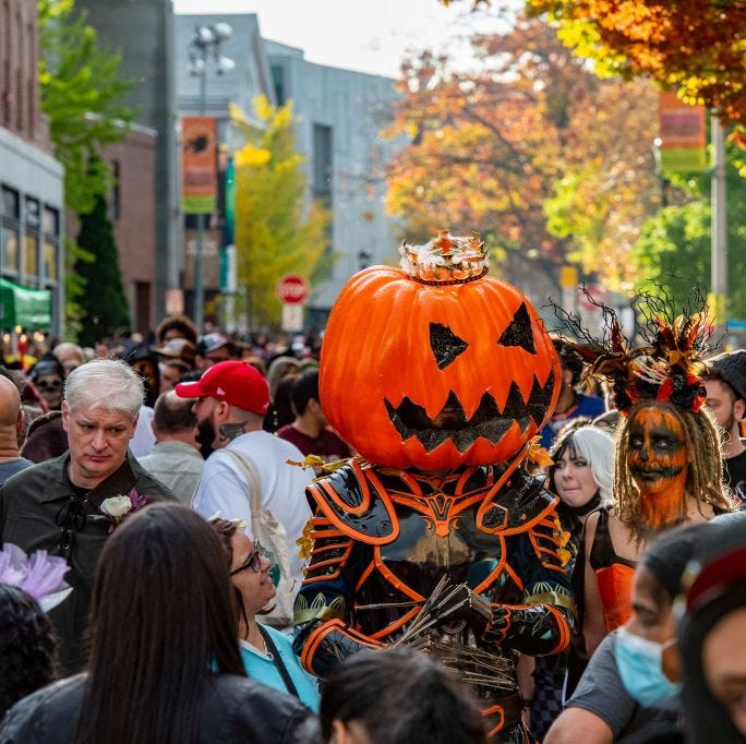 a large pumpkin headed costumed reveller walks with others through a crowded street on halloween in salem, massachusetts