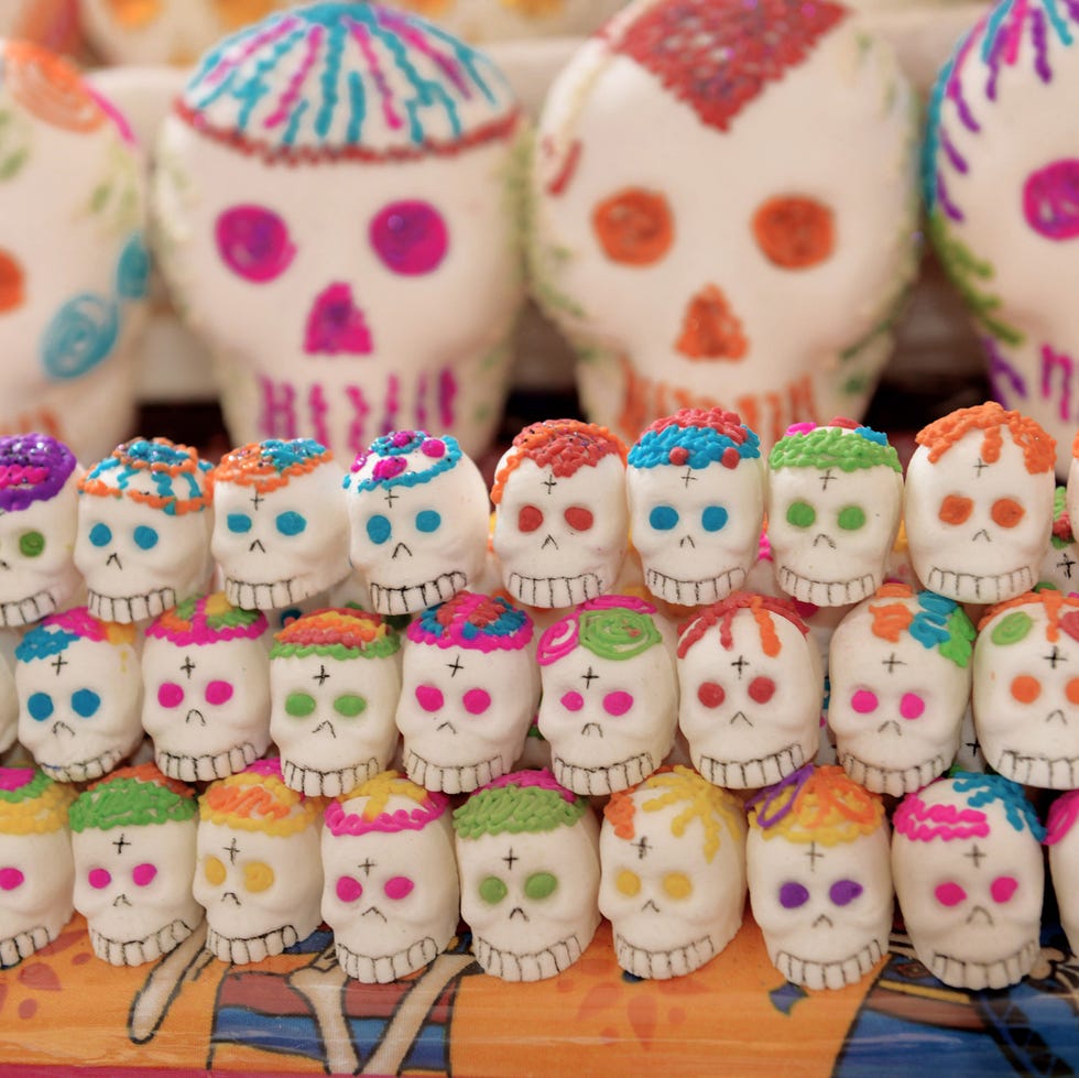 display of several rows of traditional mexican white sugar skulls decorated in various colors on sale for day of the dead celebration