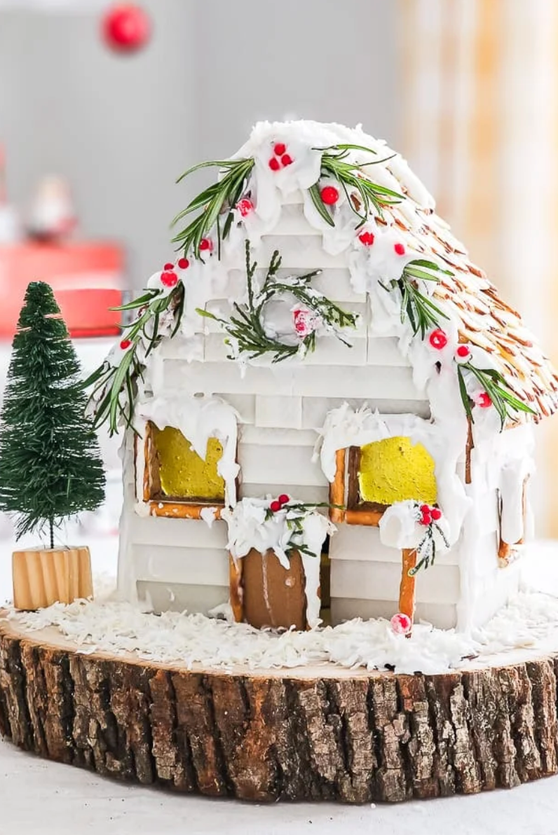 a white cottage gingerbread house with pine tree branches and candy