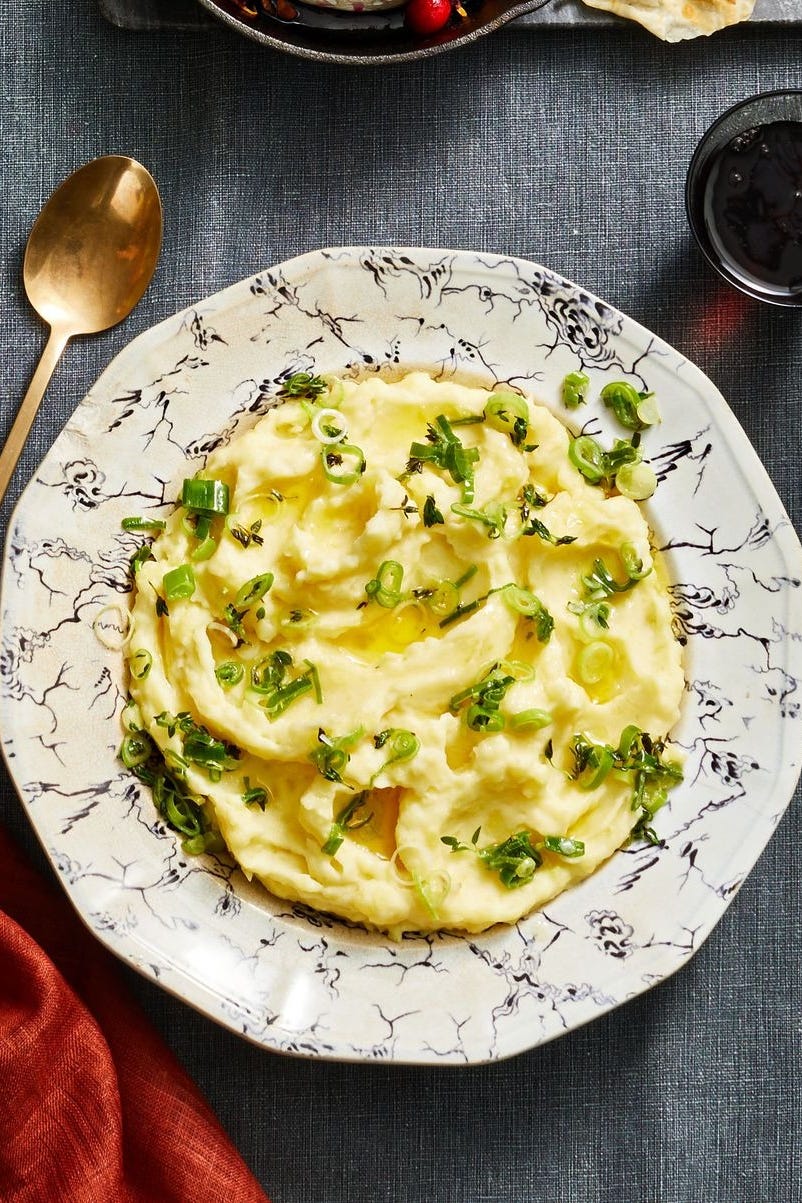 mashed potatoes with sliced scallions on top in a white bowl