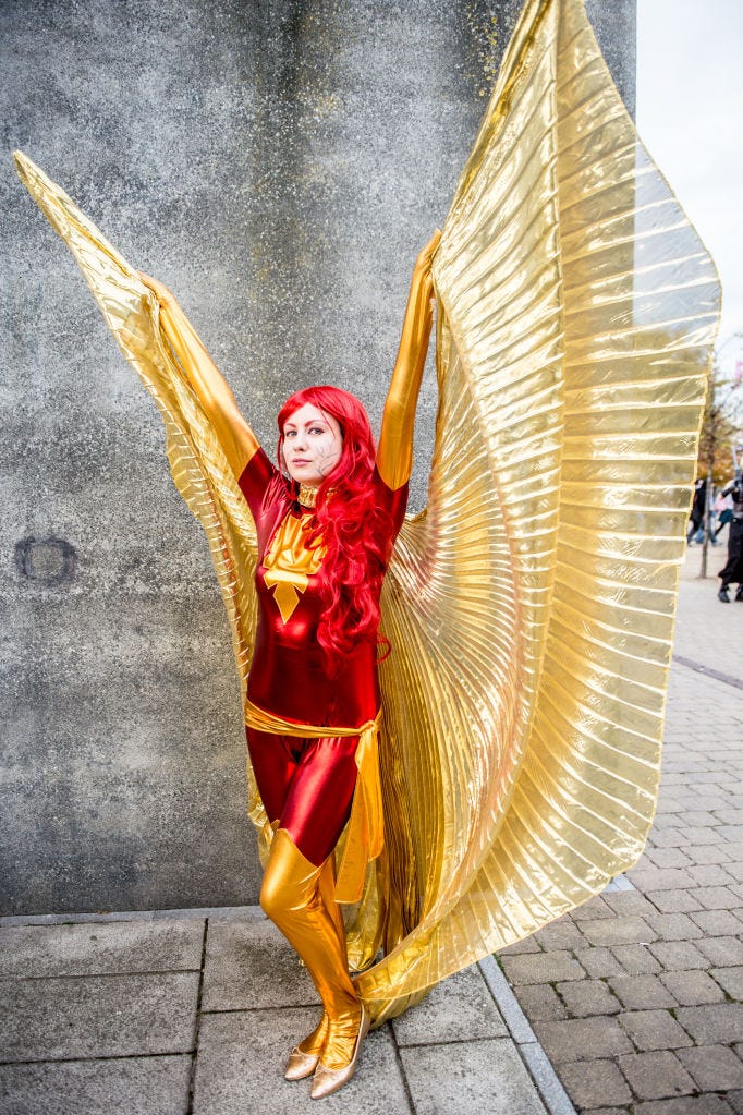 woman wearing a red bodysuit and a red wig with fake gold wings