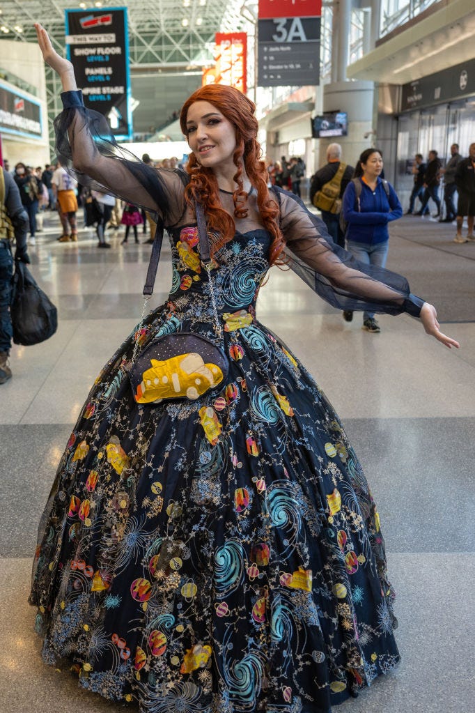 red headed woman wearing a black dress with galaxy designs and a purse with a yellow bus on it