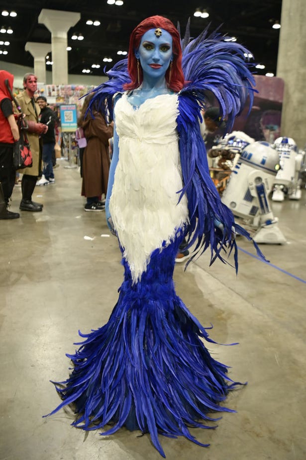 woman with red hair, blue painted skin and a feathered white and blue outfit