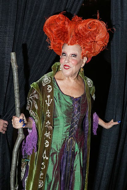 woman dressed a a red haired witch with a broom in green attire