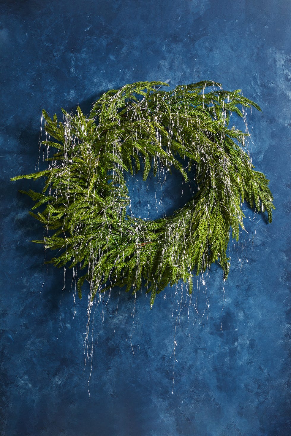 decorative wreath made of greenery and silver accents against a blue background