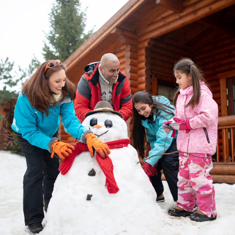 christmas activities  a multigenerational family building a snowman outside a log cabin