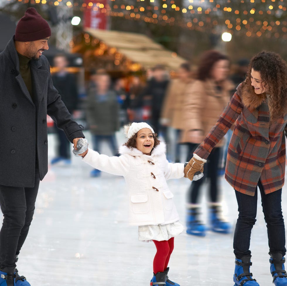 girl holding parents hands ice skating, smiling