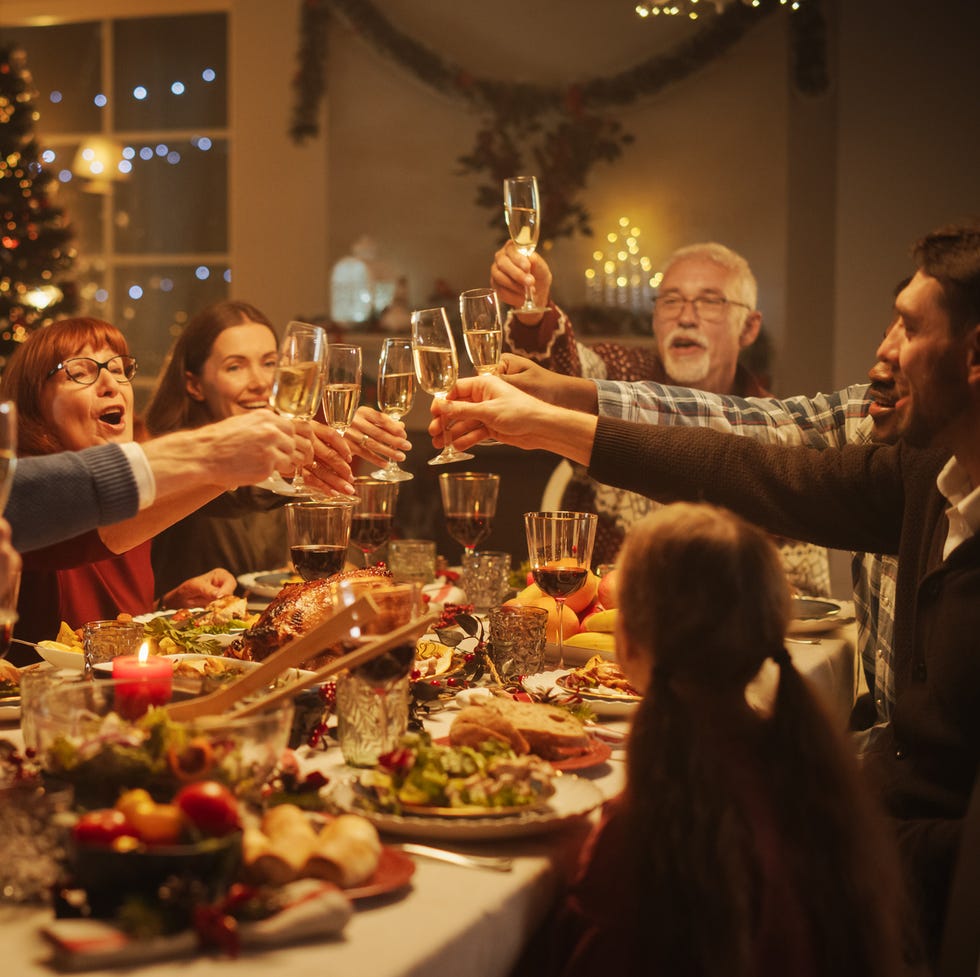 portrait of a handsome young black man proposing a toast at a christmas dinner table family and friends sharing meals, raising glasses with champagne, toasting, celebrating a winter holiday