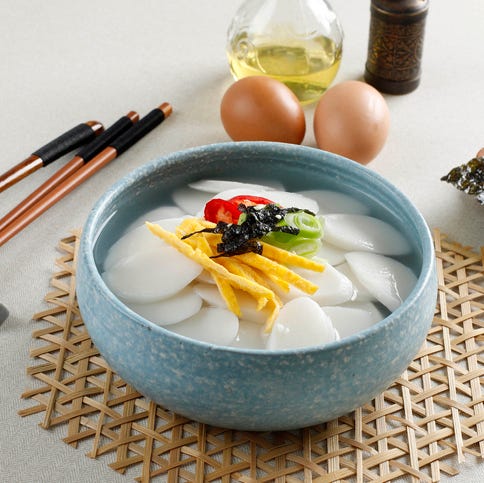 korean slice cake soup or tteokguk on blue bowl topping with egg, chilli, seaweed, and spring onion popular soup for family gathering